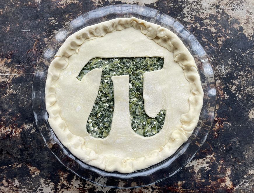 Unbaked spinach feta pie with a pi symbol cut out of the top crust