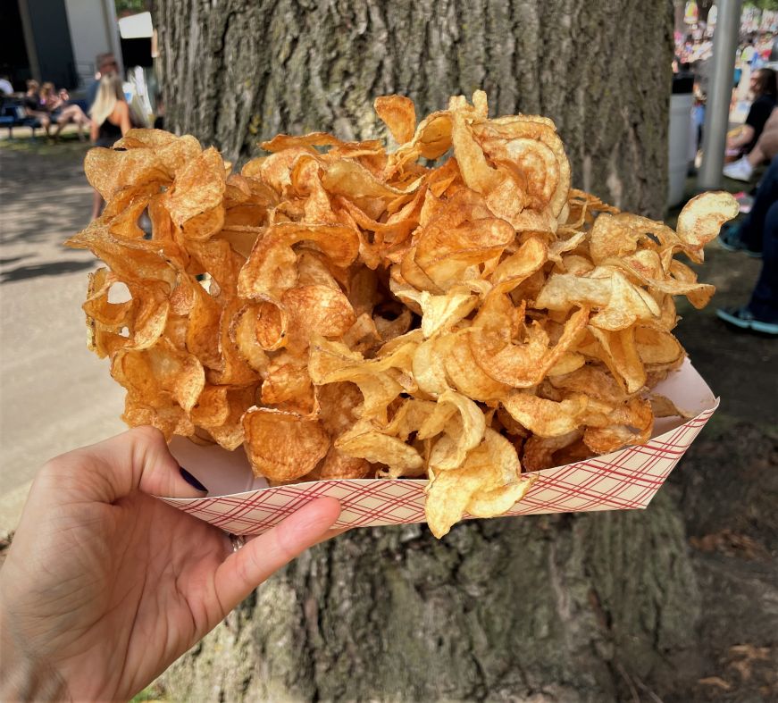 Hand holding cardboard dish heaped with spiral cut deep fried potato chips