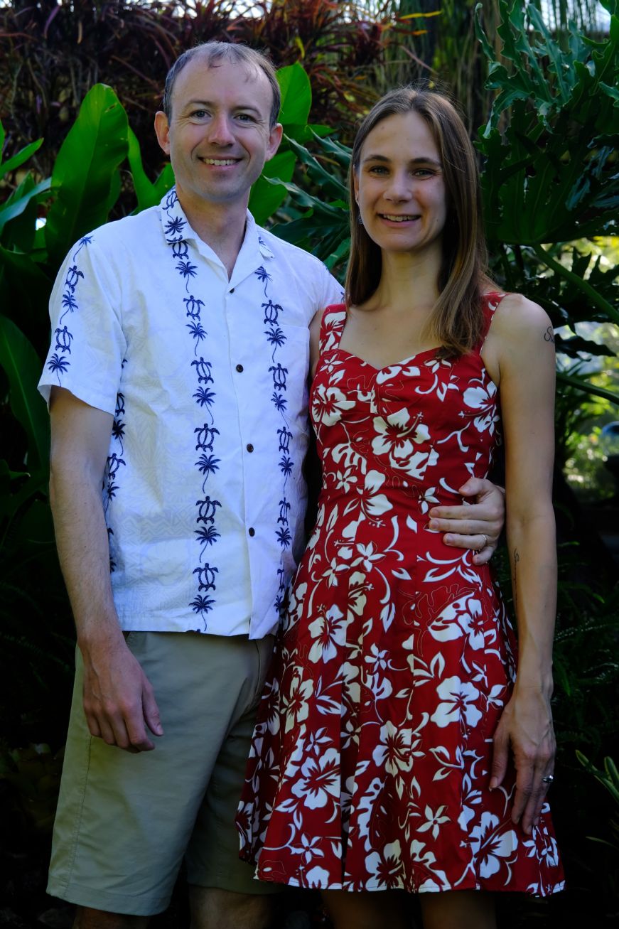 Mike wearing a white and blue aloha shirt and Stacy wearing a red dress with a white tropical flower print