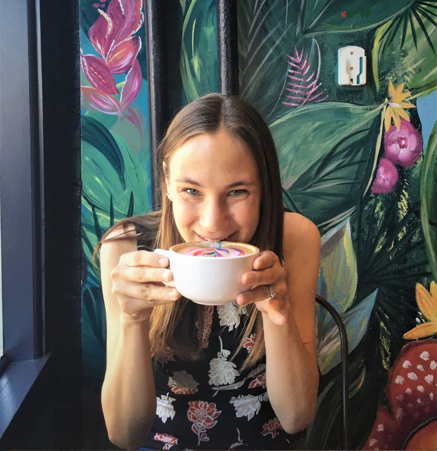 Stacy sipping a latte with a brightly colored jungle mural in the background