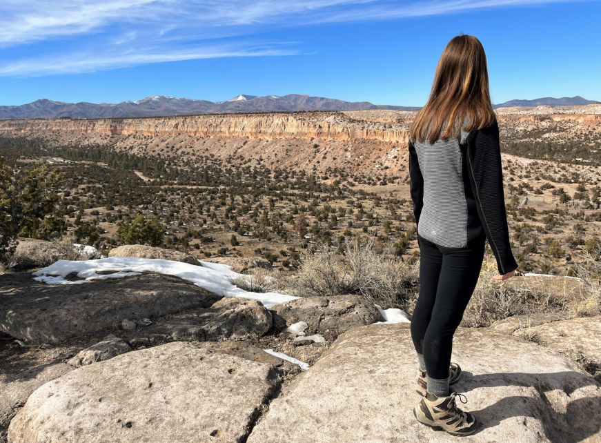Stacy standing on a mesa and looking out over a vast landscape with mesas and mountains in the distance