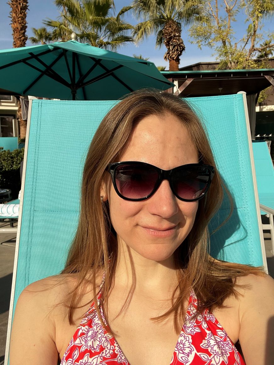Stacy wearing sunglasses and sitting in a lounge chair with palm trees in the background