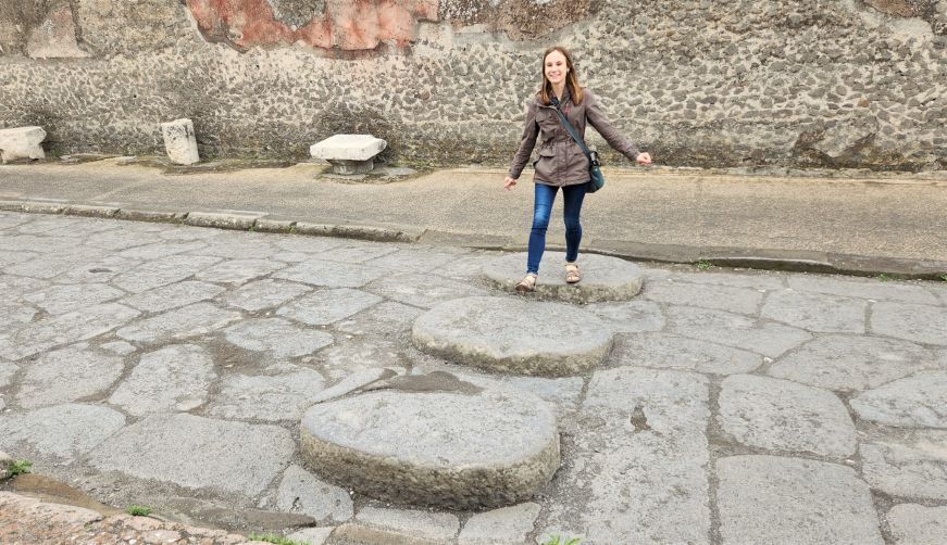 Stacy crossing a cobblestone street on a series of flat stones protruding from the street