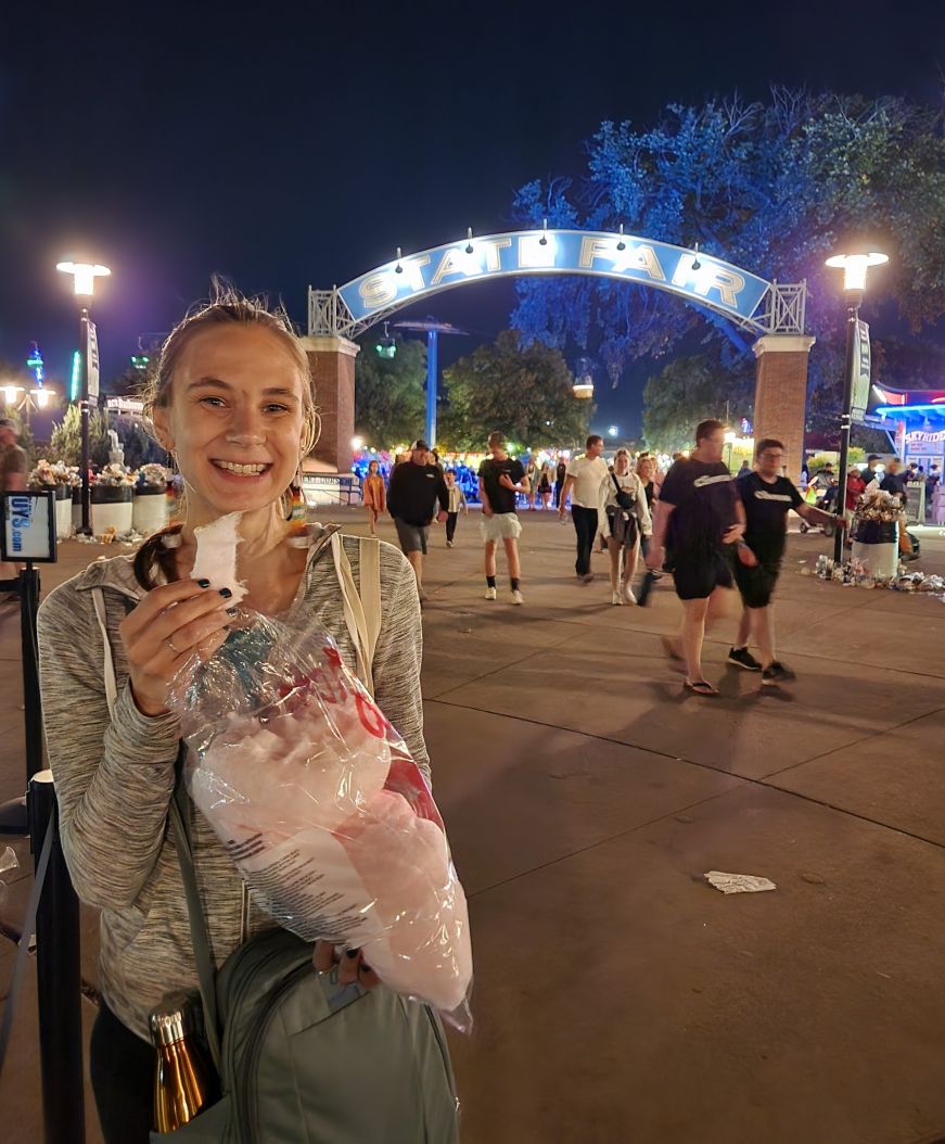 Stacy eating cotton candy by a state fair exit gate at night