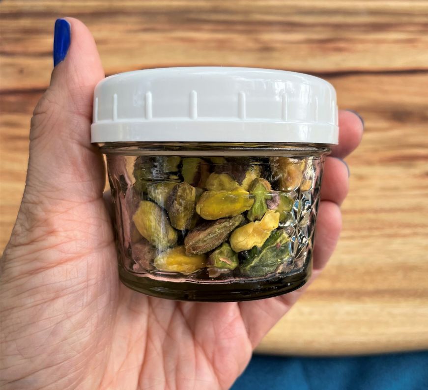 Hand holding a small glass jar of pistachios with a white plastic lid