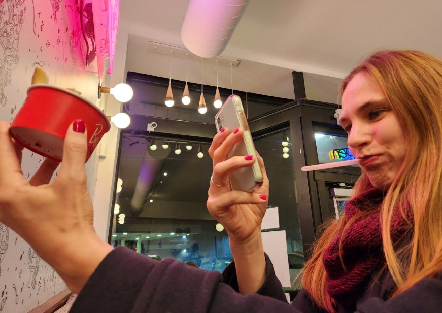 Stacy holding a cup of ice cream and taking a picture of it with her cell phone