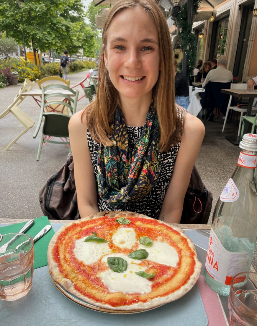 Stacy sitting at a sidewalk cafe with a margherita pizza on the table in front of her