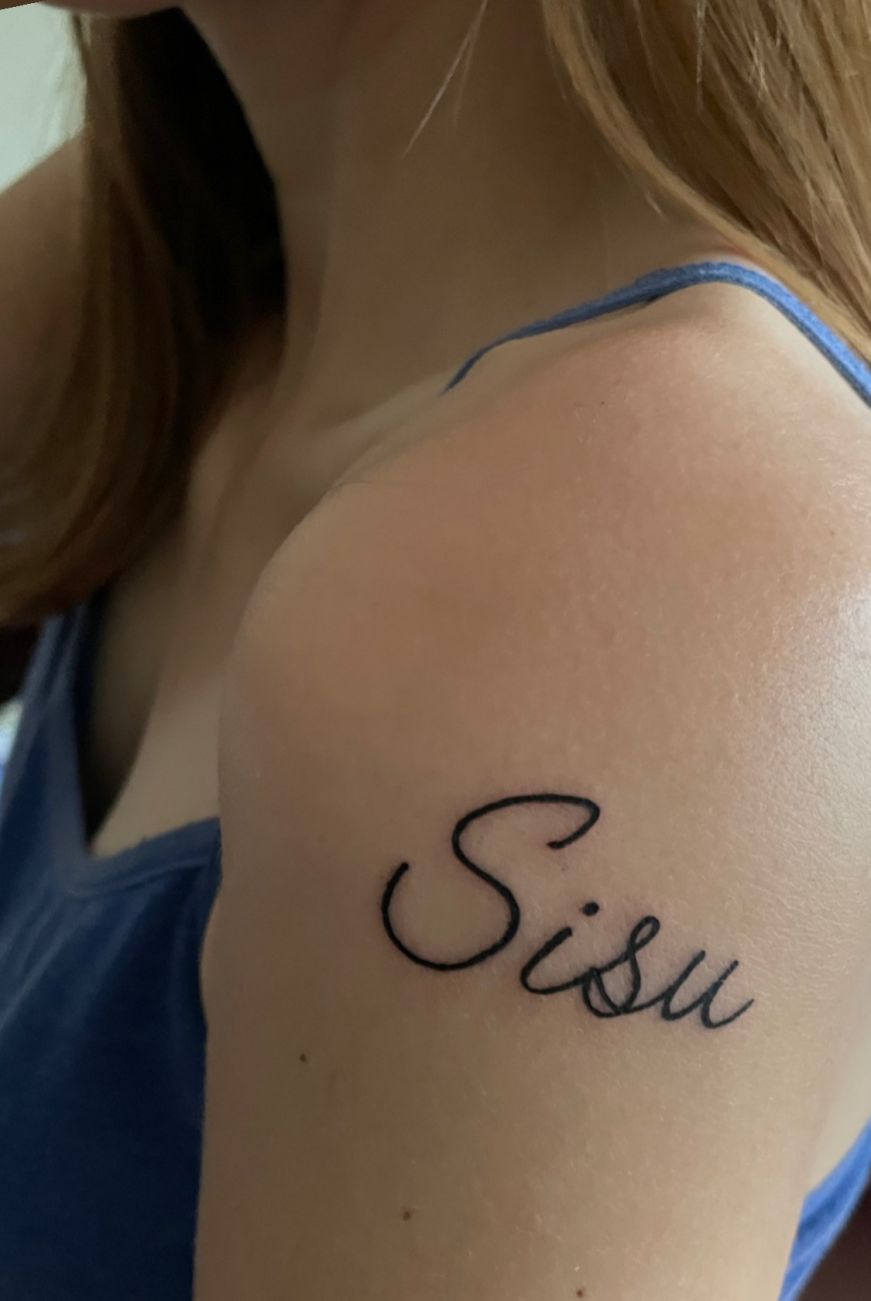 Stacy's shoulder with the word "sisu" tattooed on it in a script font