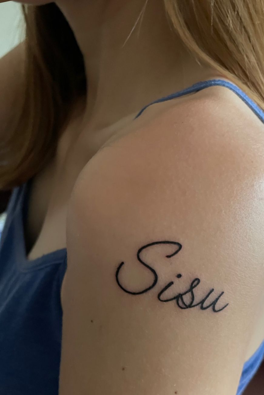 Stacy's shoulder with the word "sisu" tattooed on it in a script font
