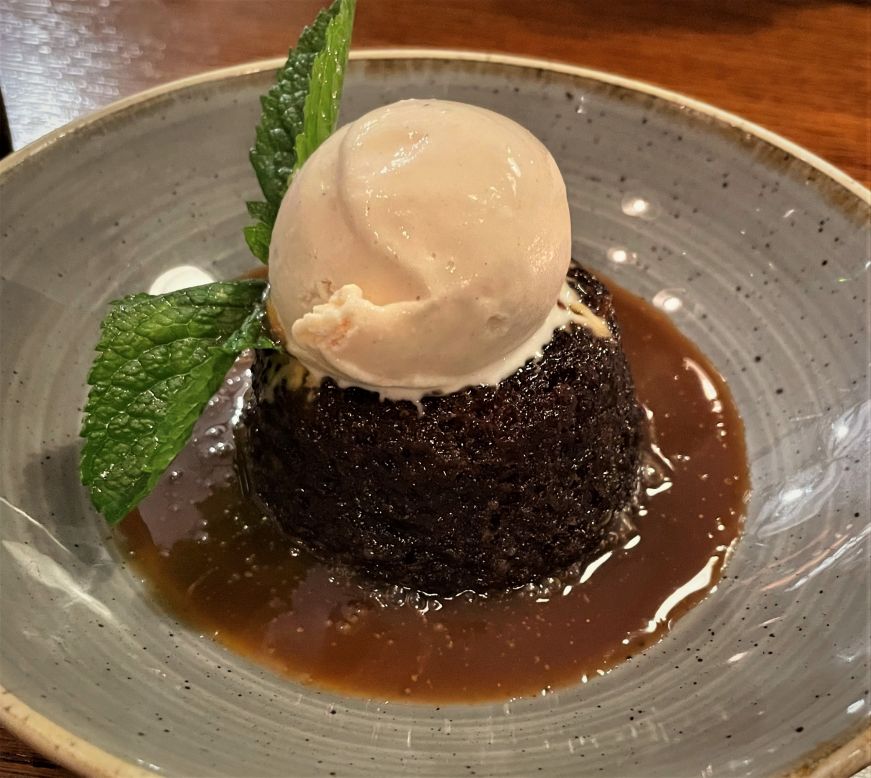 Sticky toffee pudding topped with a small scoop of vanilla ice cream