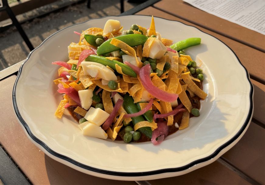 Plate of sugar snap peas topped with mole sauce, tortilla chip strips, and pieces of cheese