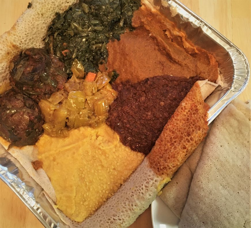 Large foil pan filled with various legume and vegetable dishes and injera