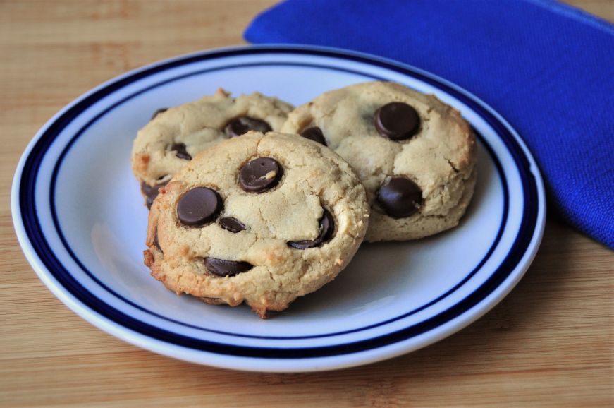 Three tahini chocolate chip cookies on a white plate with a blue edge