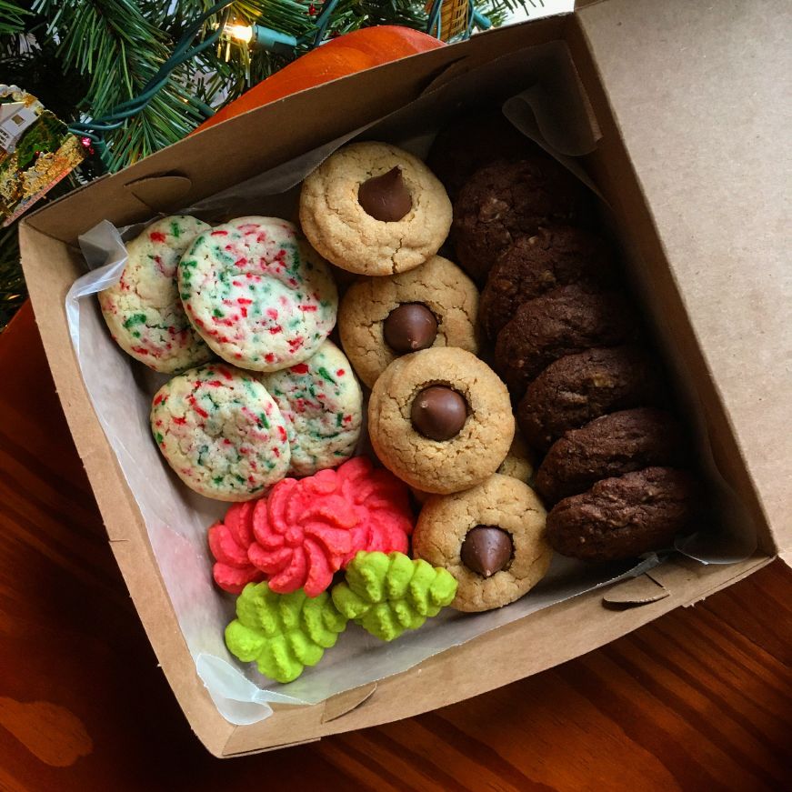 Box of holiday cookies next to a Christmas tree