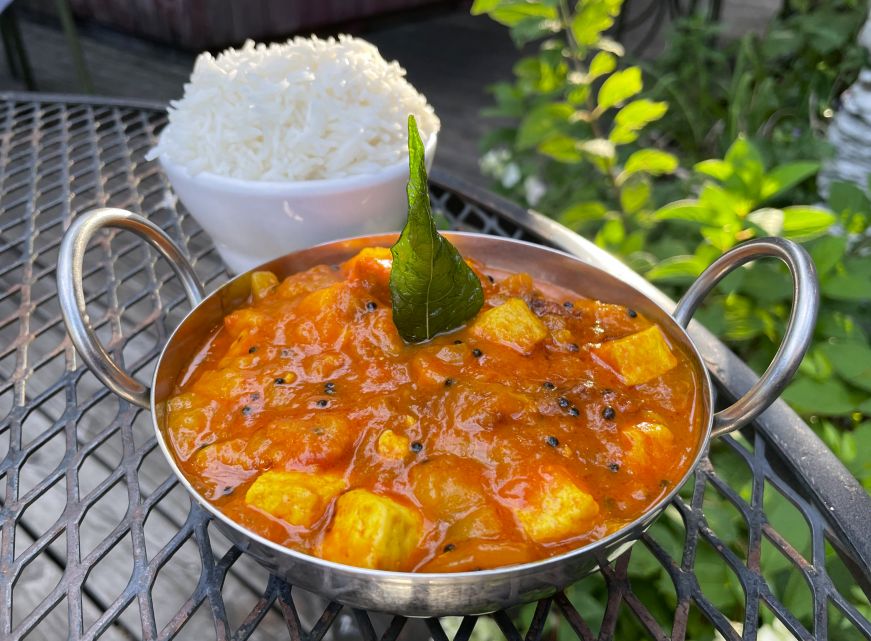 Tangy mango curry with tofu, Namaste Cafe Metal dish of tofu in a bright mango curry sauce with a bowl of rice in the background