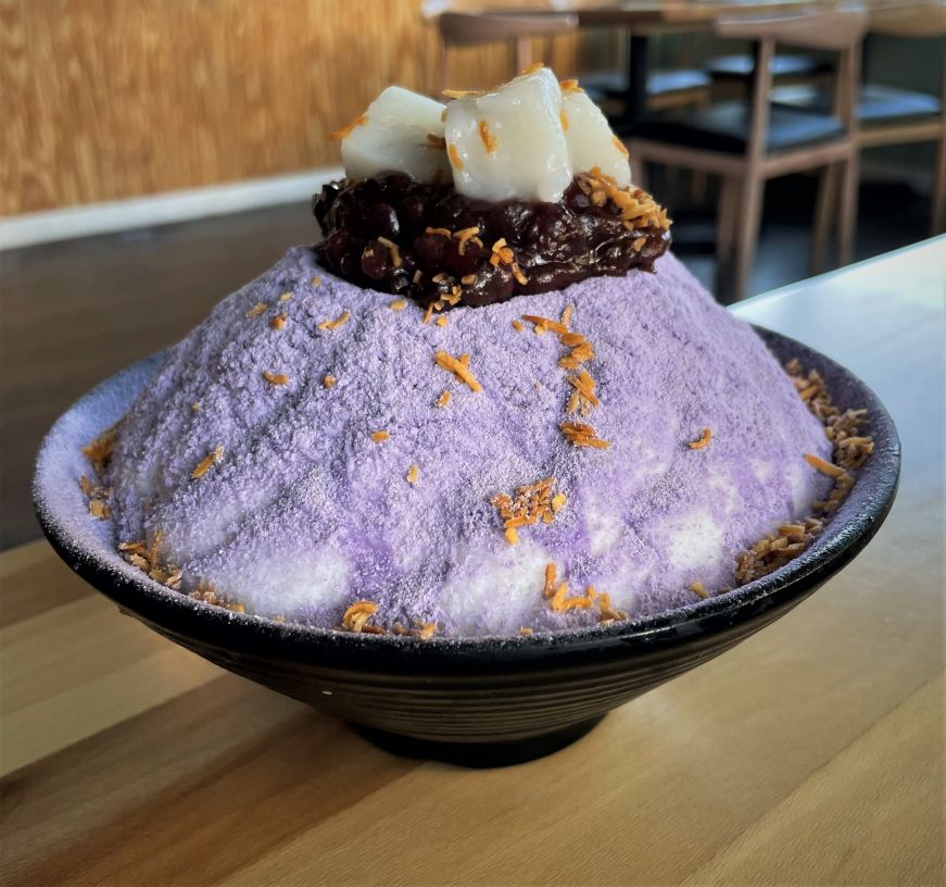 Large bowl of shave ice topped with lavendar taro powder, red bean paste, toasted coconut, and small cubes of rice cake