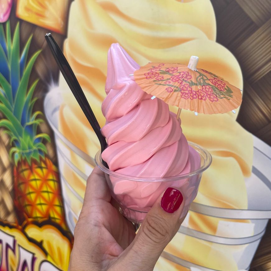 Stacy's hand holding a cup of pink soft serve garnished with a paper umbrella