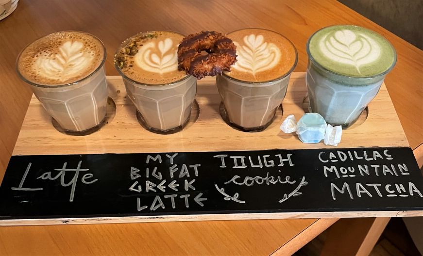 Flight of four small glasses containing lattes with latte art