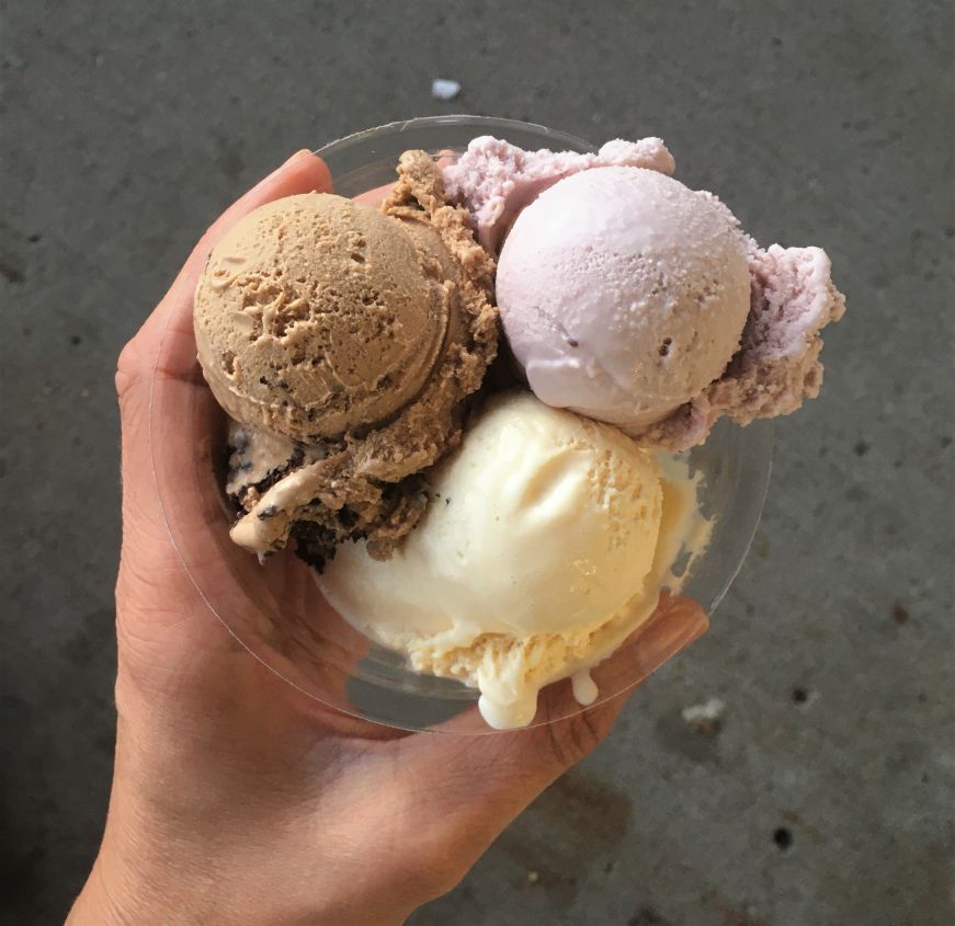 Hand holding clear plastic dish with three small scoops of ice cream