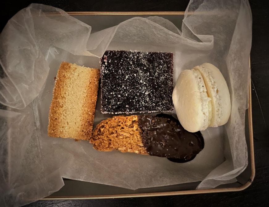 Small metal box containing a macaron, biscotti, shortbread cookie, and fruit jelly