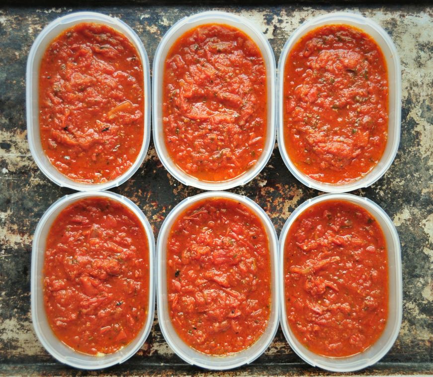 Six plastic containers filled with tomato sauce