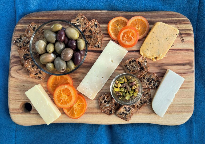 Top down view of a cheese board with olives, crackers, nuts, and dried oranges