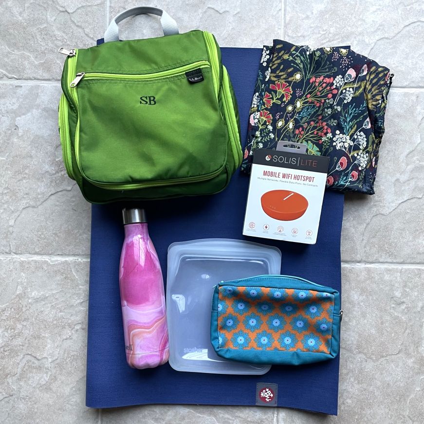 Top down view of toiletry bag, water bottle, and other recommended travel products arranged on a folded yoga mat