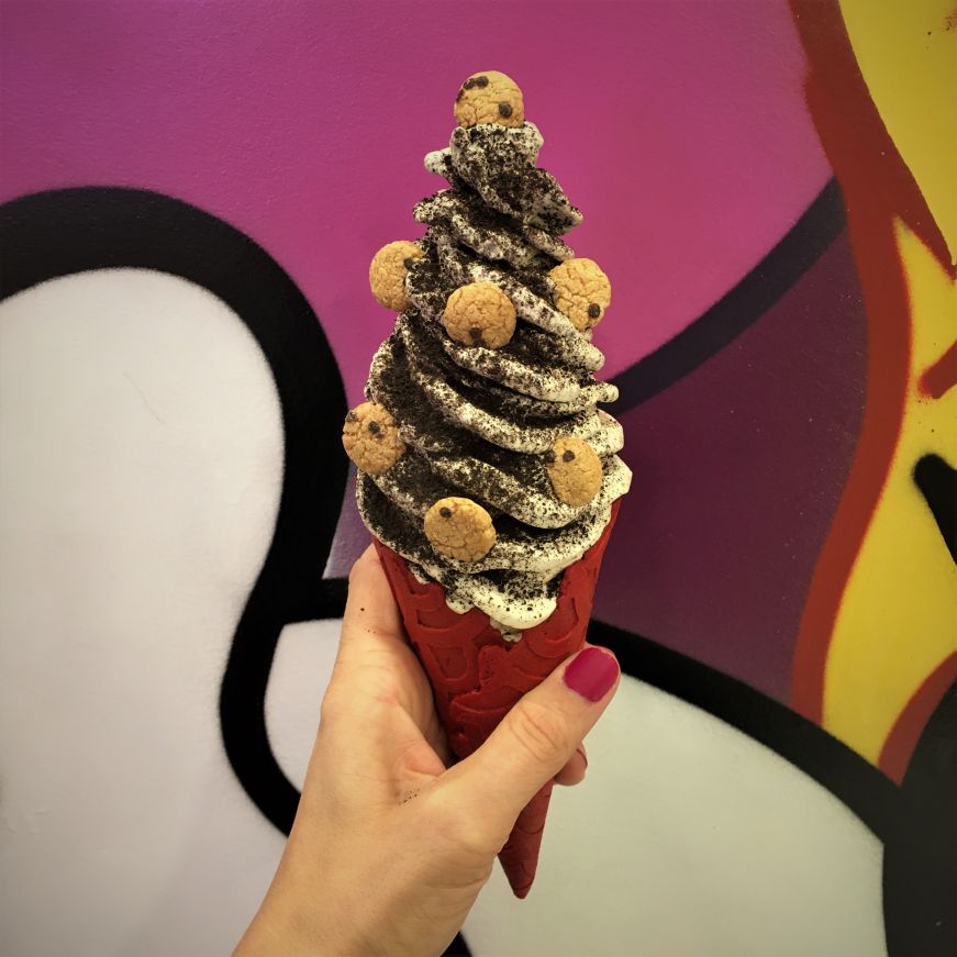 Hand holding soft serve cone garnished with Oreo crumbs and pieces of cereal