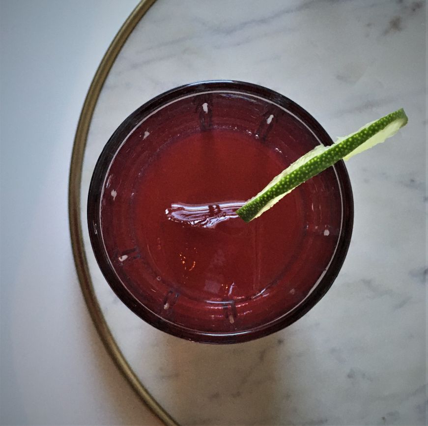 Top down view of a purple cocktail garnished with a lime slice on a marble tray