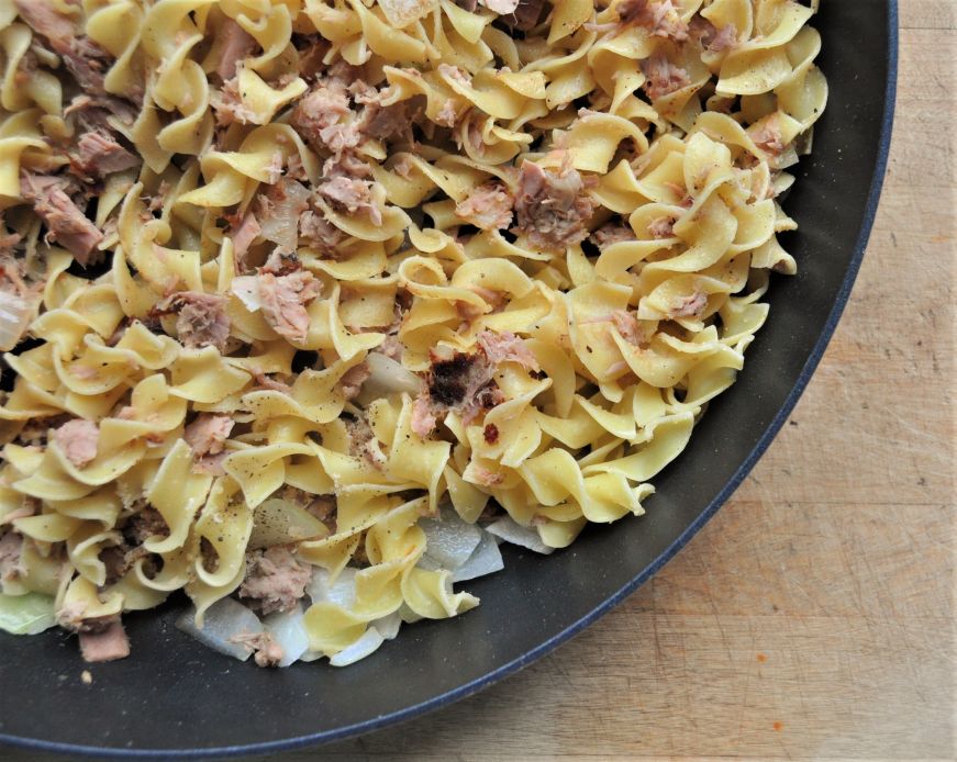 Close up view of egg noodles and canned tuna in a skillet