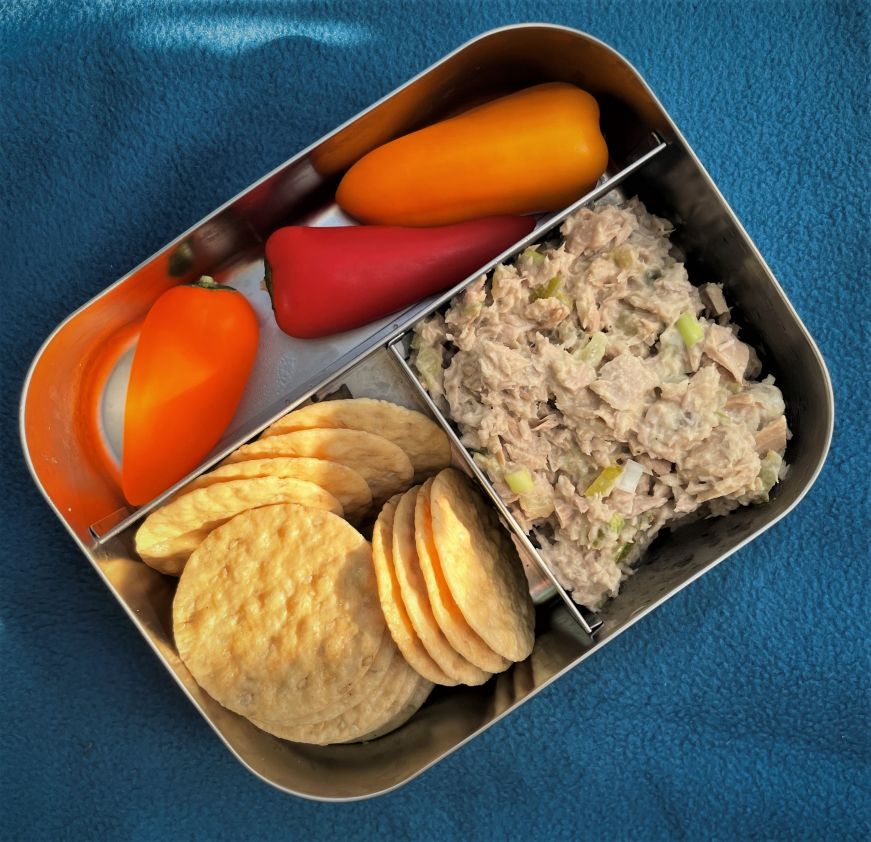 Metal bento box with compartments holding miniature bell peppers, crackers, and tuna salad