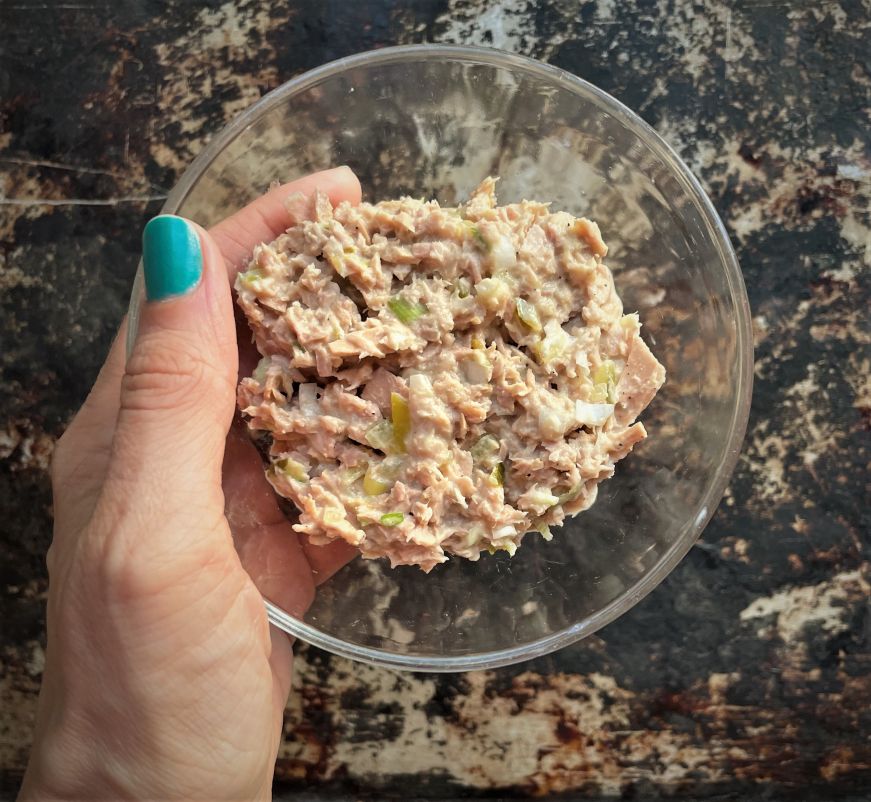 Hand holding small glass bowl filled with tuna salad