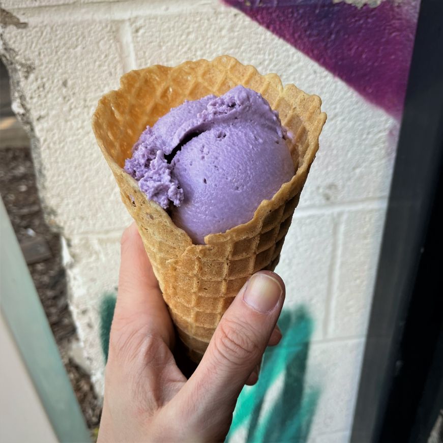Hand holding waffle cone with a scoop of purple ice cream