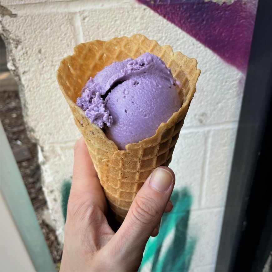 Ube ice cream at Crepe & Spoon Hand holding waffle cone with a scoop of purple ice cream