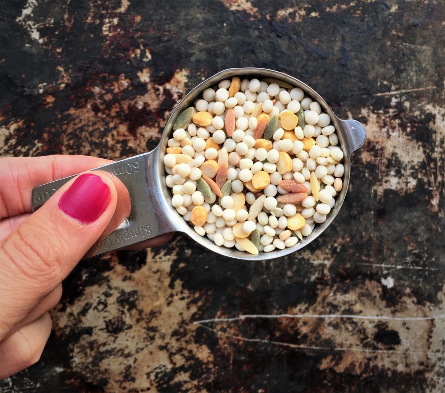 Top down view of a hand holding a measuring cup with uncooked Harvest Grains Blend