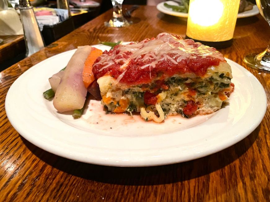 A plate with a large piece of vegetable lasagna with carrots and green beans on the side