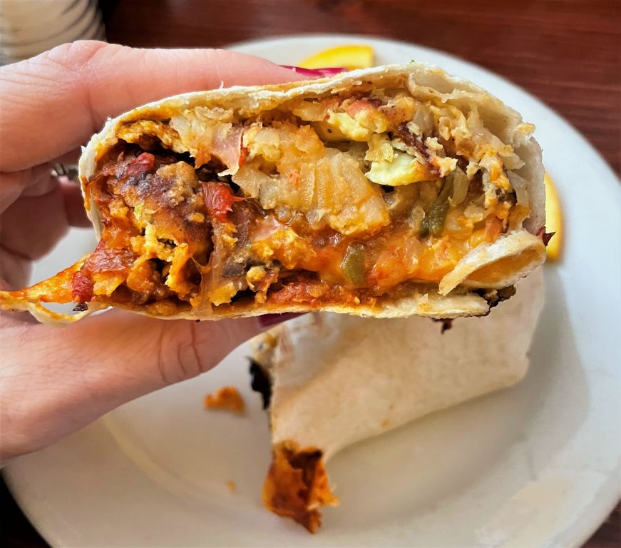 Hand holding half of a veggie breakfast burrito