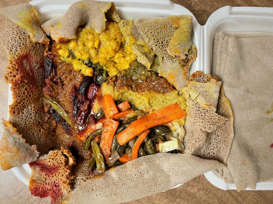 Styrofoam takeout container filled with injera, vegetable dishes, and lentil stews