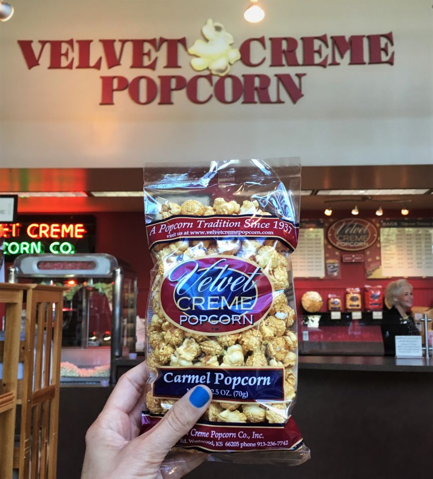 Hand holding bag of carmel popcorn up against Velvet Creme Popcorn sign, Kansas City, Kansas