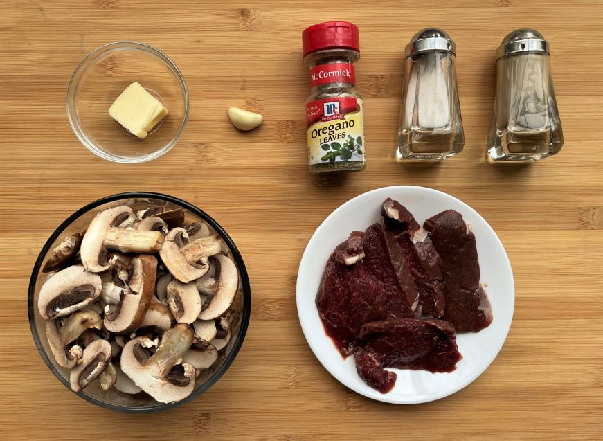 Venison tenderloin with garlicky mushrooms ingredients arranged on wooden cutting board