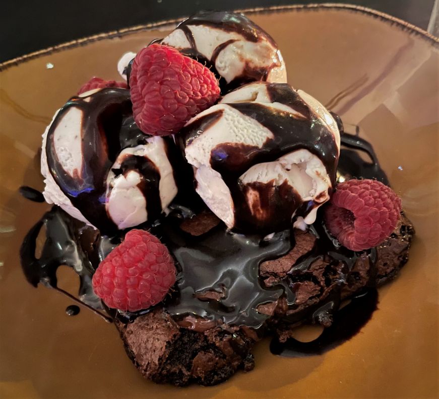 Brownie topped with small scoops of vanilla gelato, hot fudge, and fresh raspberries