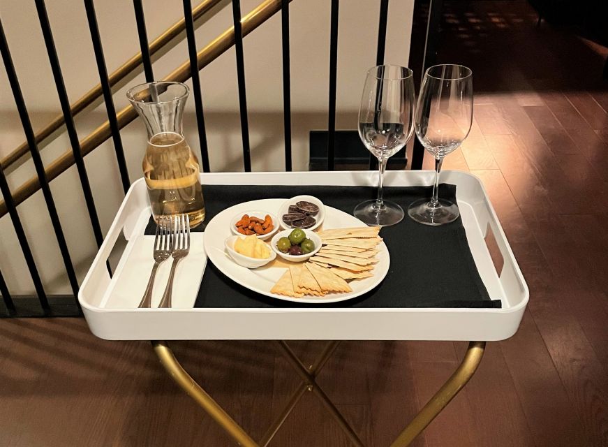 White tray with wine glasses, carafe of white wine, and a plate with olives, crackers, almonds, cheese, and chocoalte