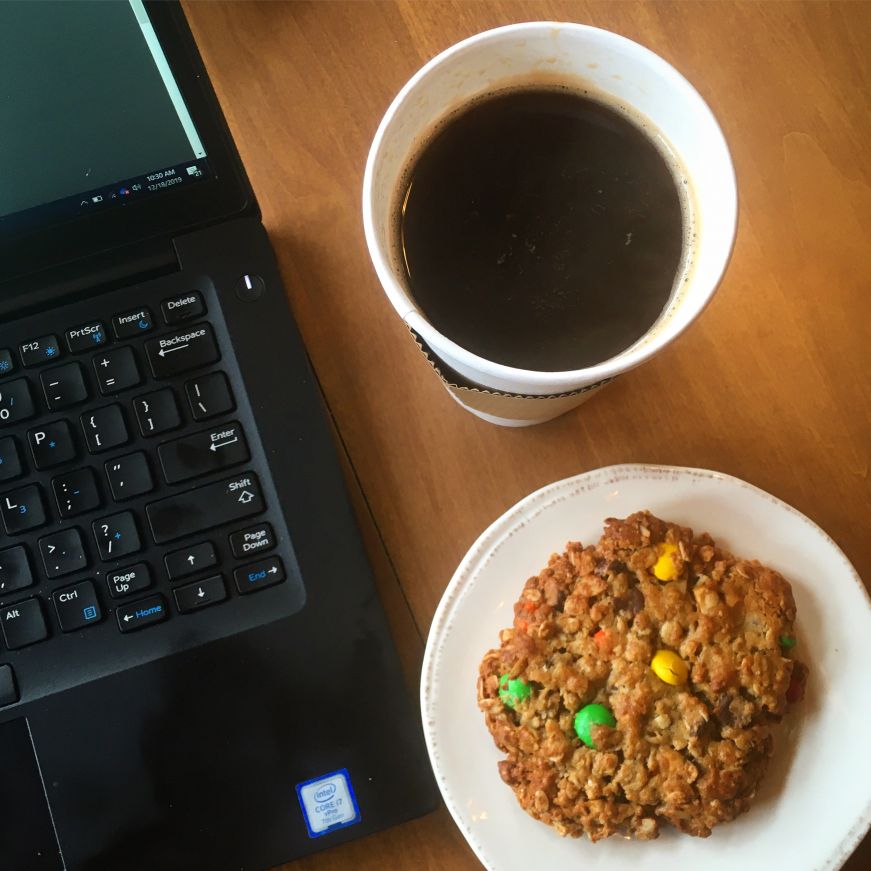 Top down view of laptop keyboard, cup of coffee, and oatmeal M&M cookie