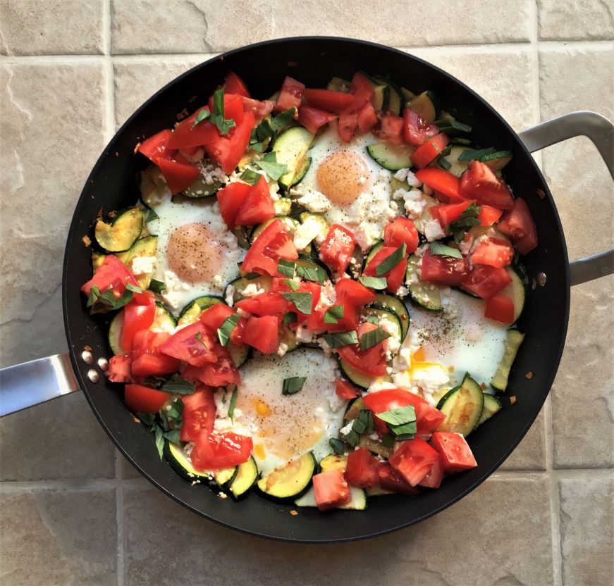 Skillet filled with zucchini, tomatoes, and four eggs