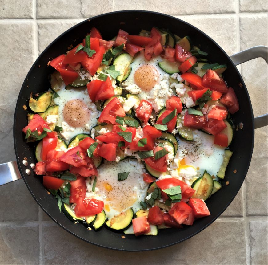 Skillet filled with sauteed zucchini, eggs, and tomatoes