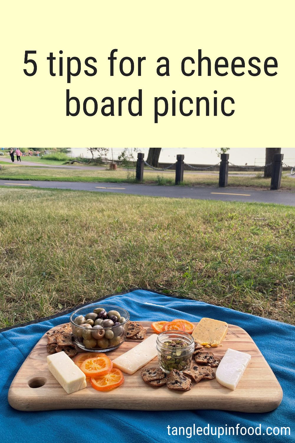 Photo of cheese board on picnic blanket with text reading "5 tips for a cheese board picnic"