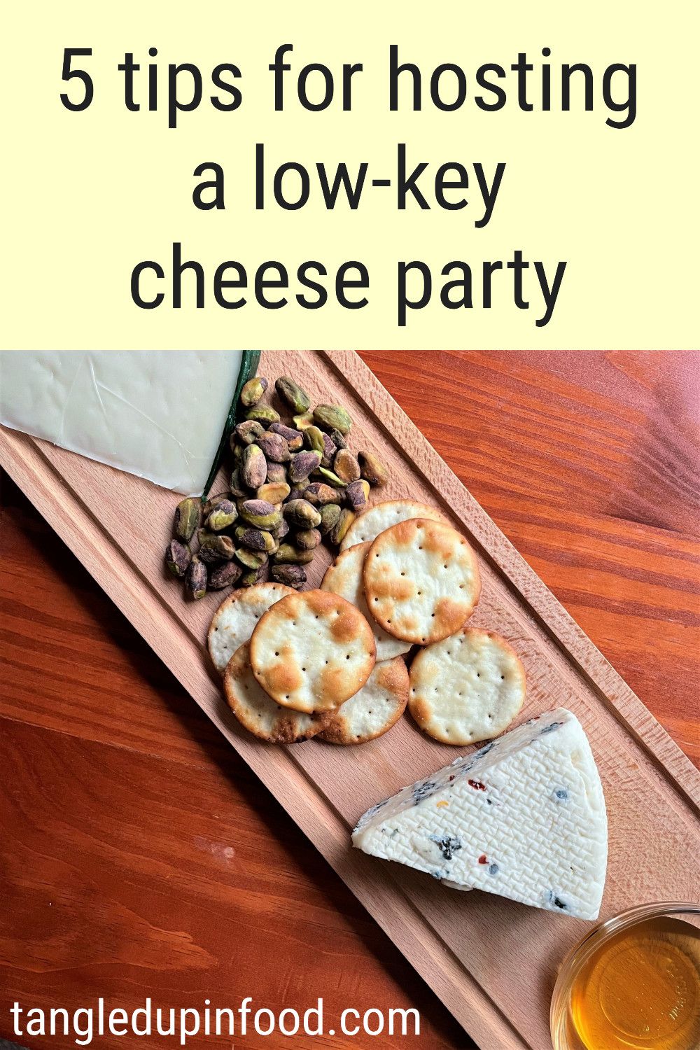 Cheese board with a wedge of blue cheese, pistachios, crackers, and a small bowl of honey and text reading "5 tips for hosting a low-key cheese party"