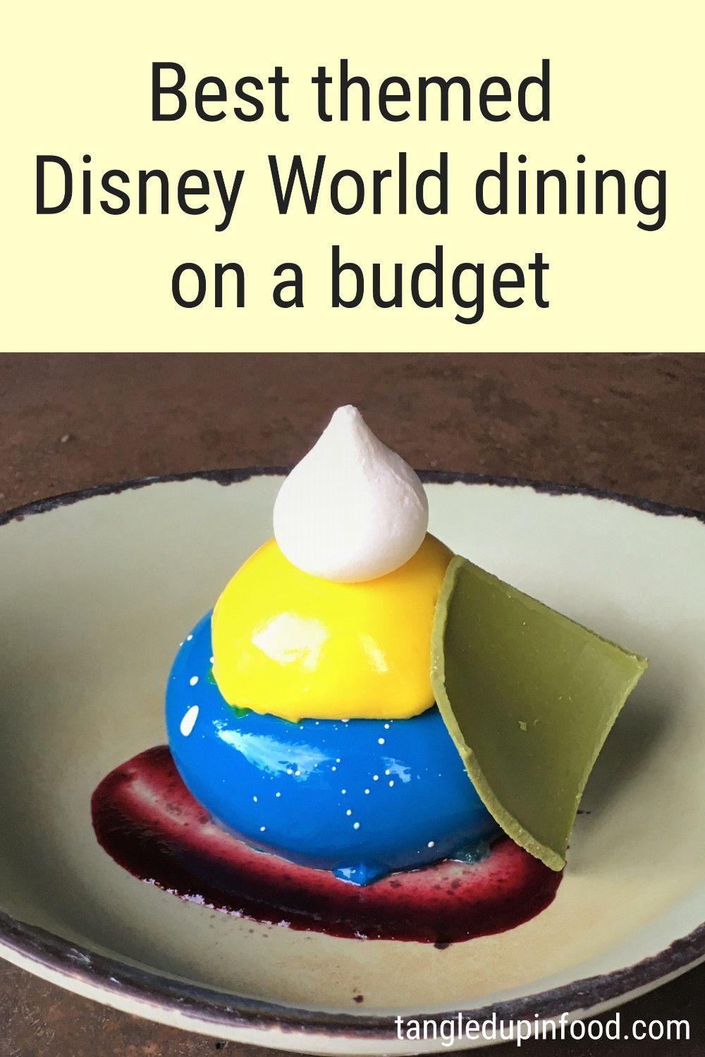 Bright blue mousse cake garnished with a bright yellow topping and meringue dollop and text reading "Best themed Disney World dining on a budget"