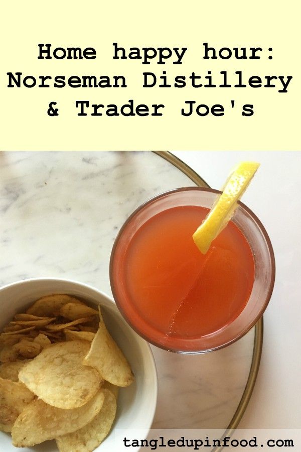 Top down view of cocktail garnished with lemon slice and bowl of potato chips with text reading "Home happy hour: Norseman Distillery and Trader Joe's"