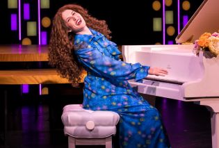 Woman with long curly hair playing a piano and singing